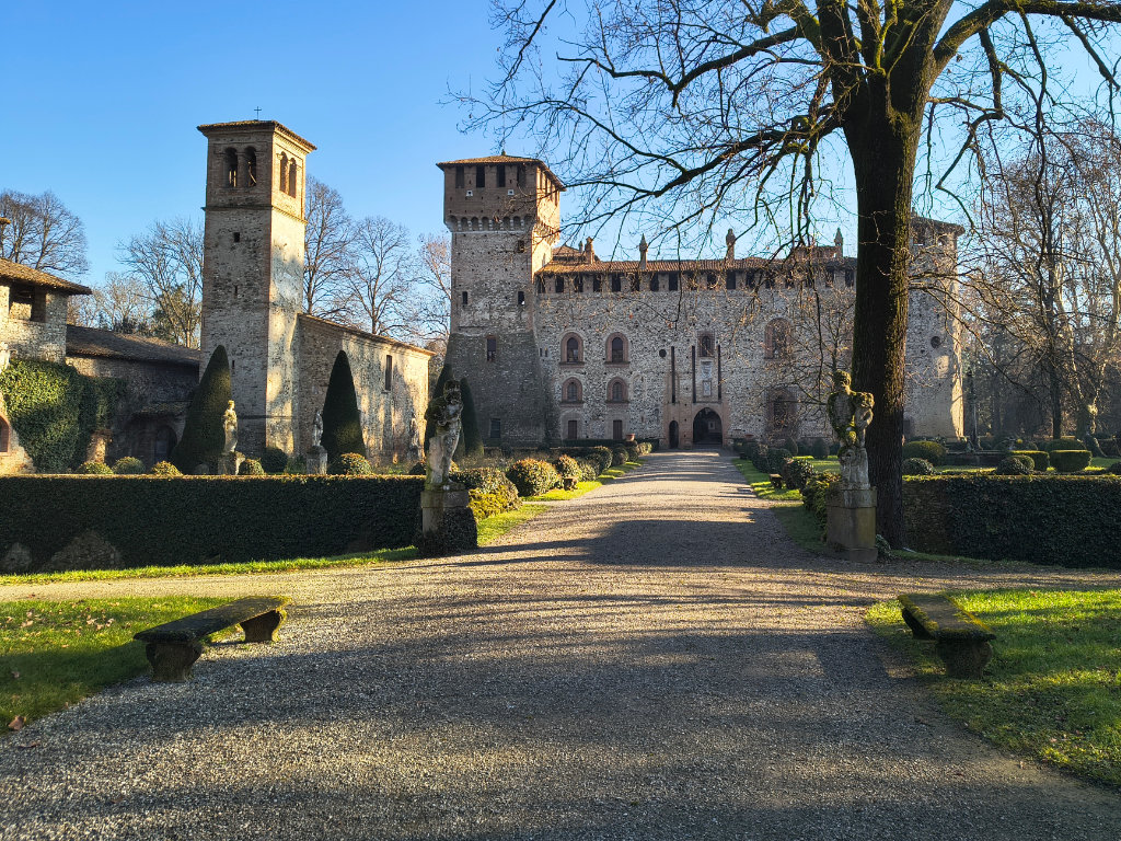 La facciata del castello di Grazzano con la chiesa e il campanile visti dal giardino con alberi, siepi e statue